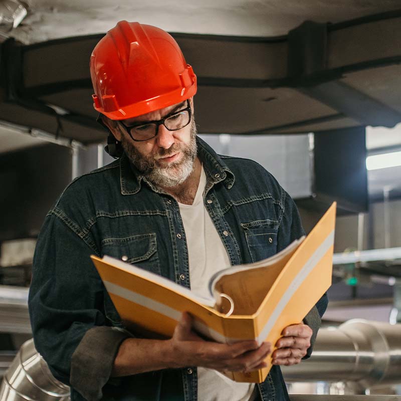 Man wearing red hard hat looking through a yellow binder