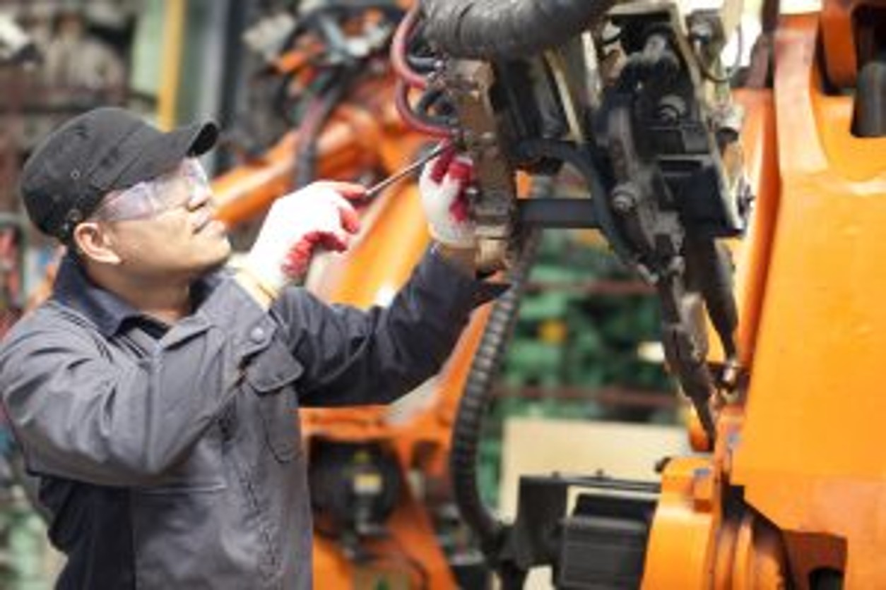 A technician wearing protective gear while screwing a machine component