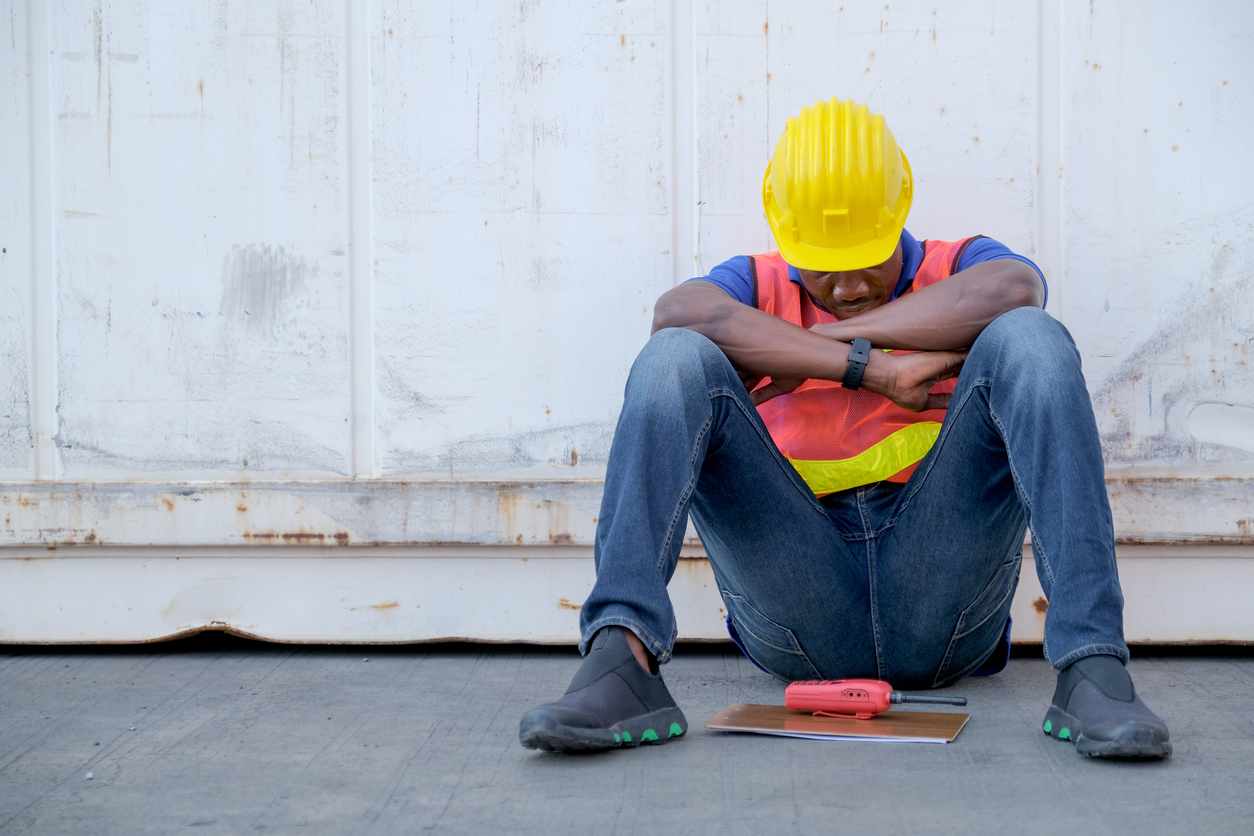 A technician sitting on the ground with head down seemingly stopping work due to machine failure