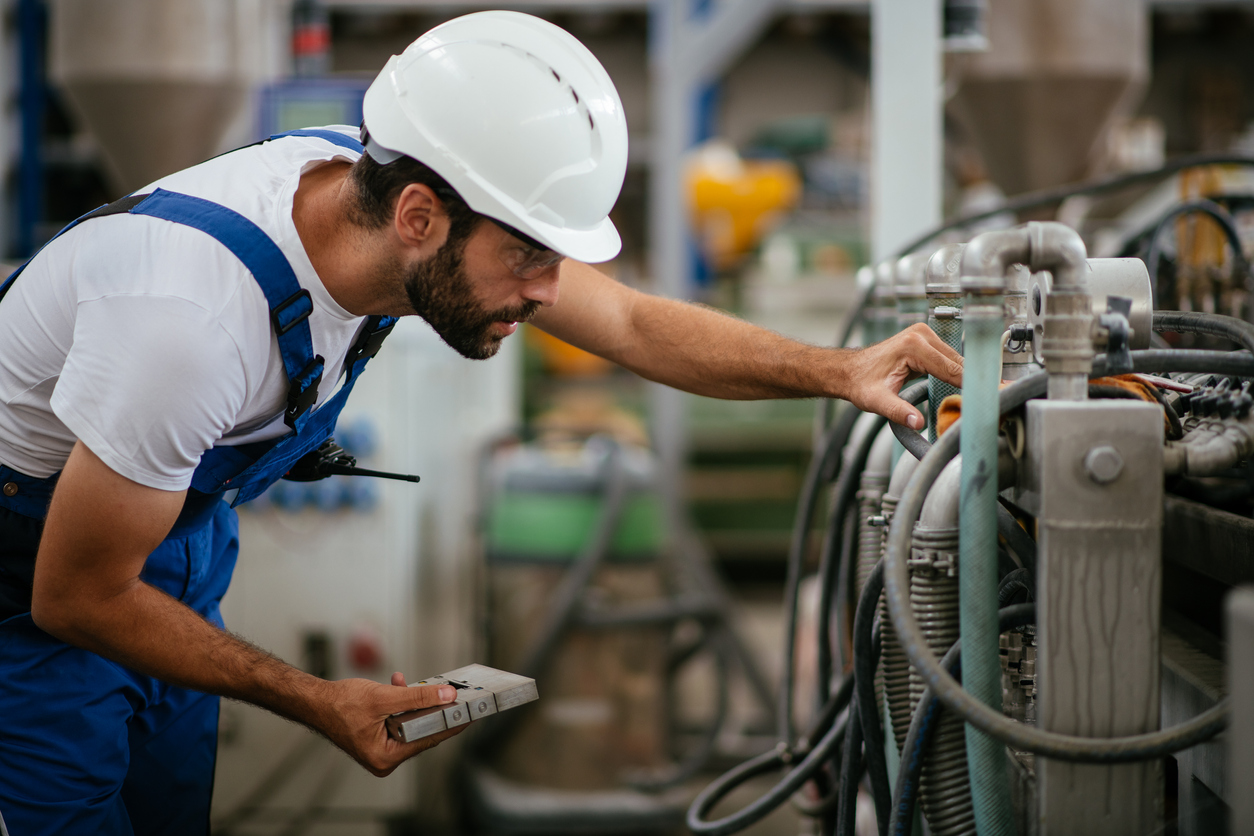 An industrial machine maintenance worker bends over to inspect a component on a heavy machine