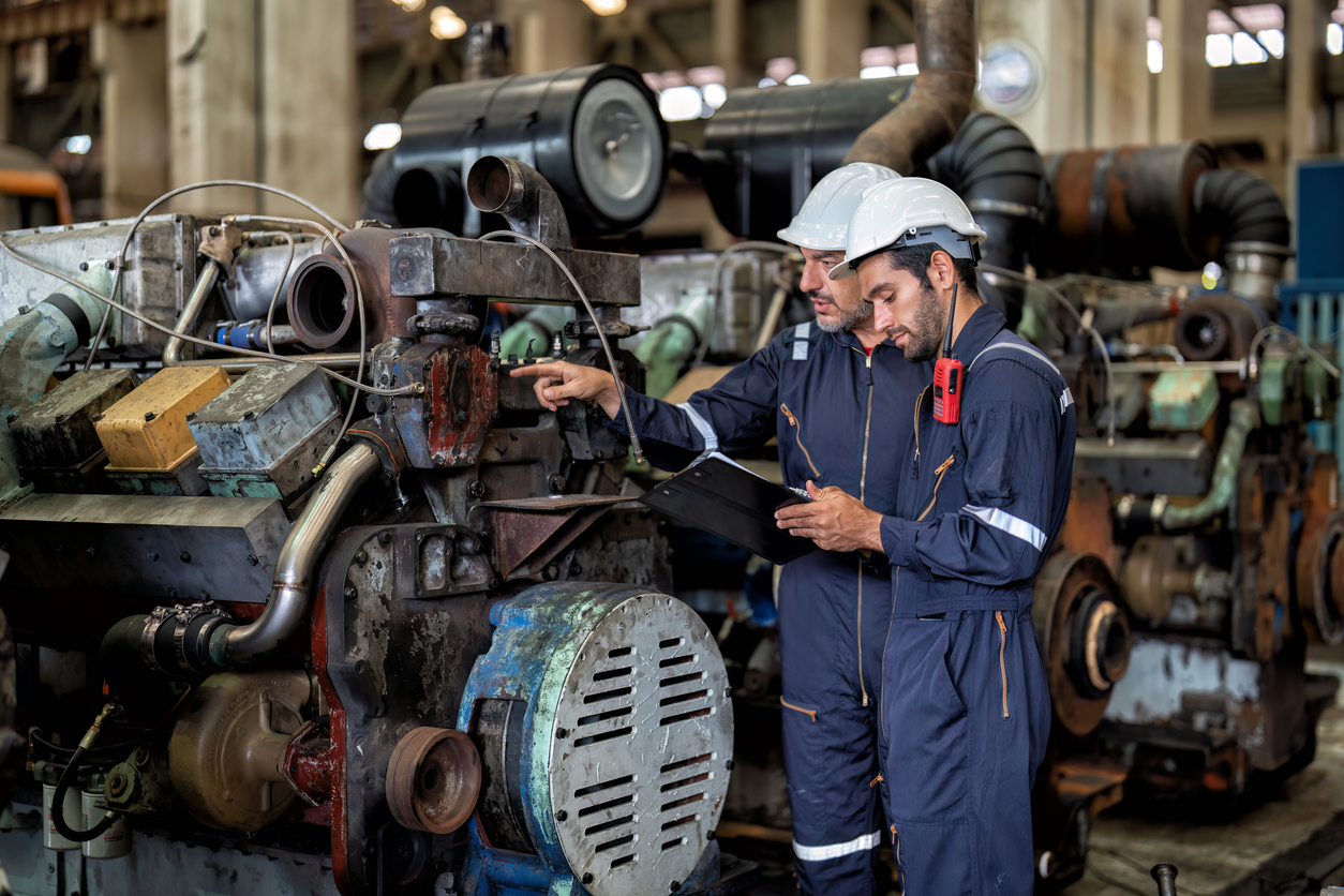 A maintenance tech & machine operator look over a piece of heavy industrial equipment