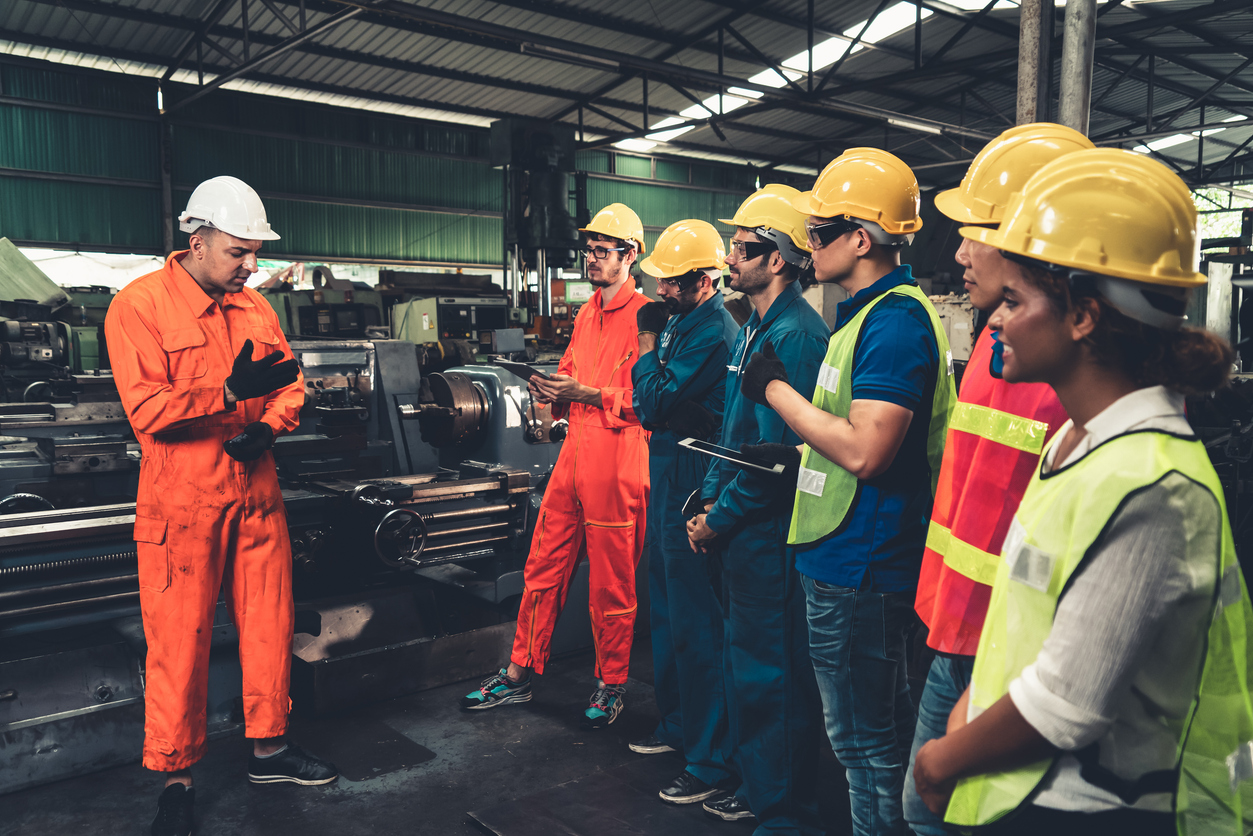 A heavy machine maintenance tech explains his findings to workers in hard hats