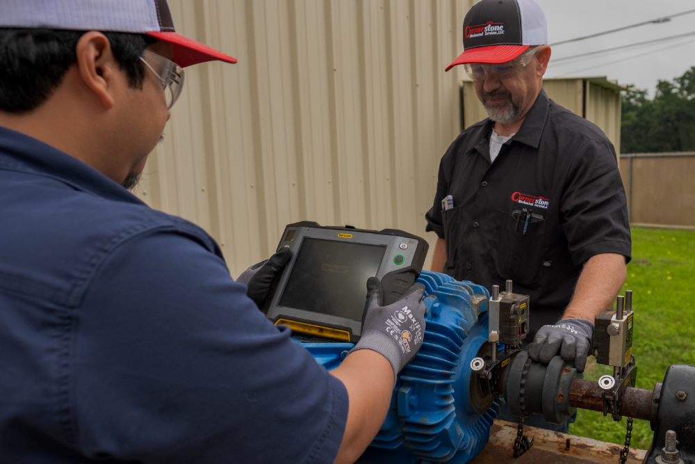 Two technicians in work uniforms inspect a blue industrial pump with a digital tablet outdoors, conveying skilled, hands-on maintenance.